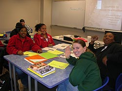 Four students sitting around a table with two waving